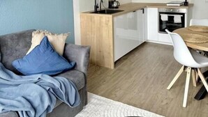 Een moderne woonkamer met een grijze bank, een salontafel en een eethoek met een houten tafel en witte stoelen.