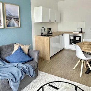 Ein modernes Wohnzimmer mit grauem Sofa, einem Couchtisch und einem Essbereich mit Holztisch und weißen Stühlen.