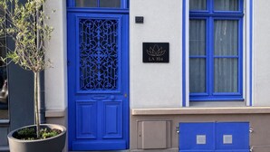 Un bâtiment avec une porte bleue, un pot de fleurs et une enseigne ornée d’un symbole de lotus.