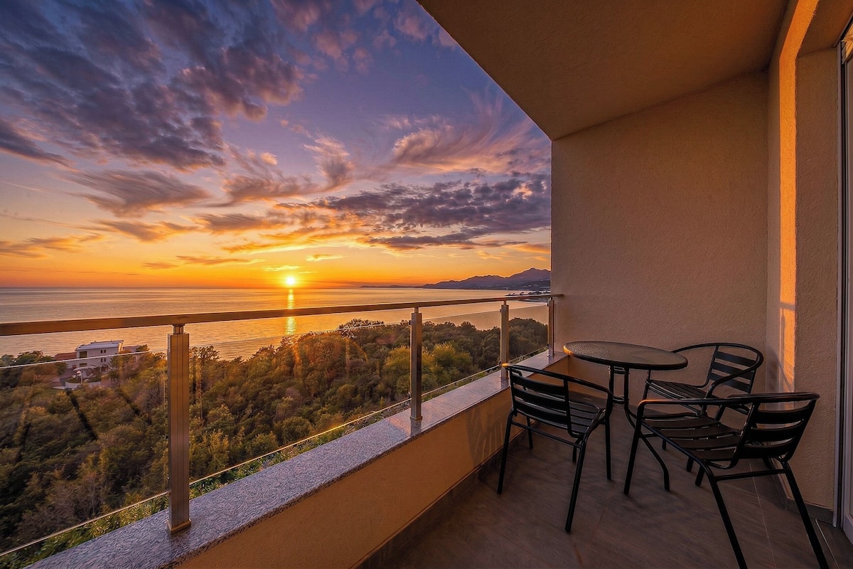 Un balcon avec vue sur le coucher de soleil sur la mer, une table et des chaises.
