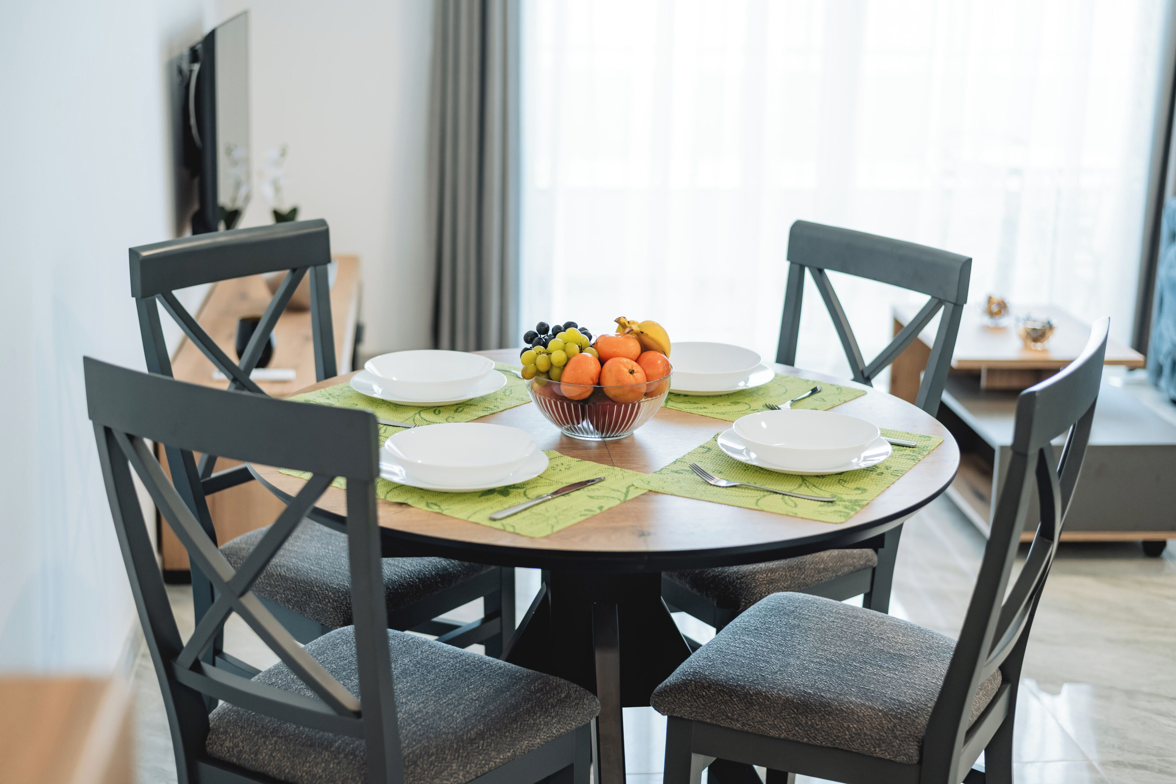 A dining table with a fruit bowl, plates, and cutlery, surrounded by chairs.