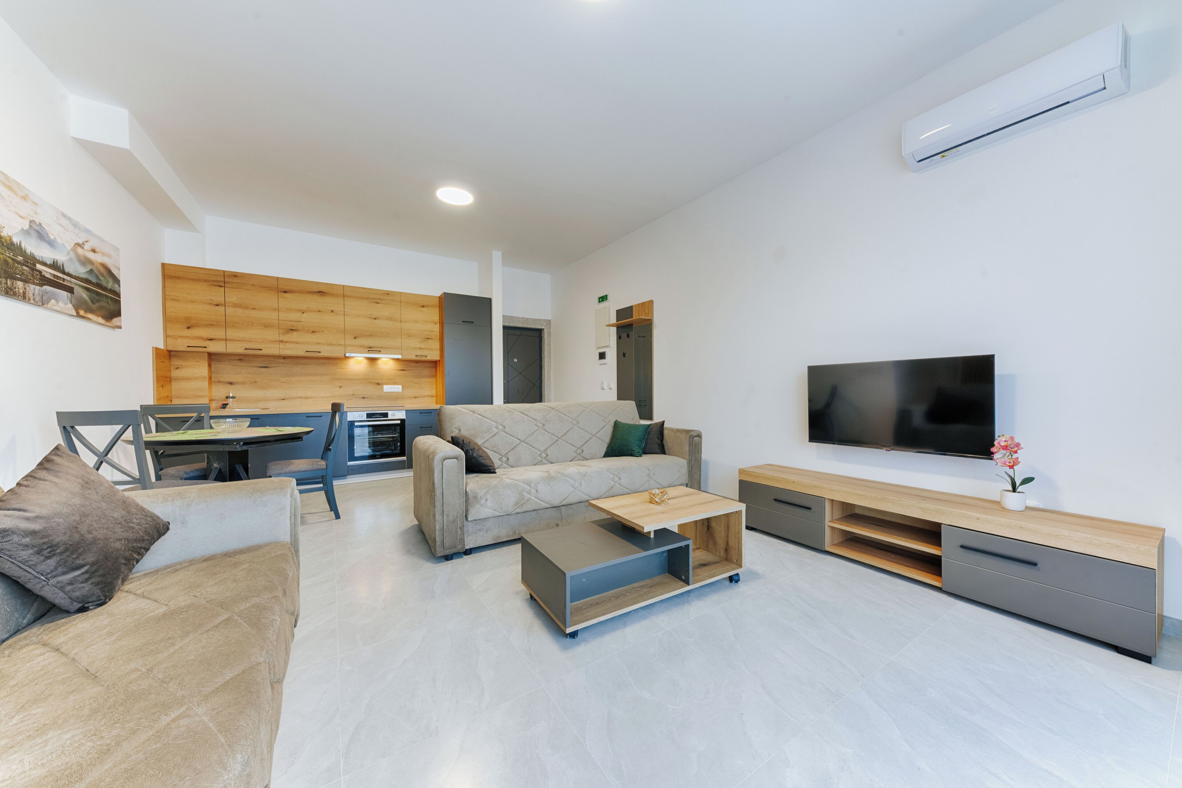 A modern living room with a sofa, coffee table, TV, and a kitchen area in the background.