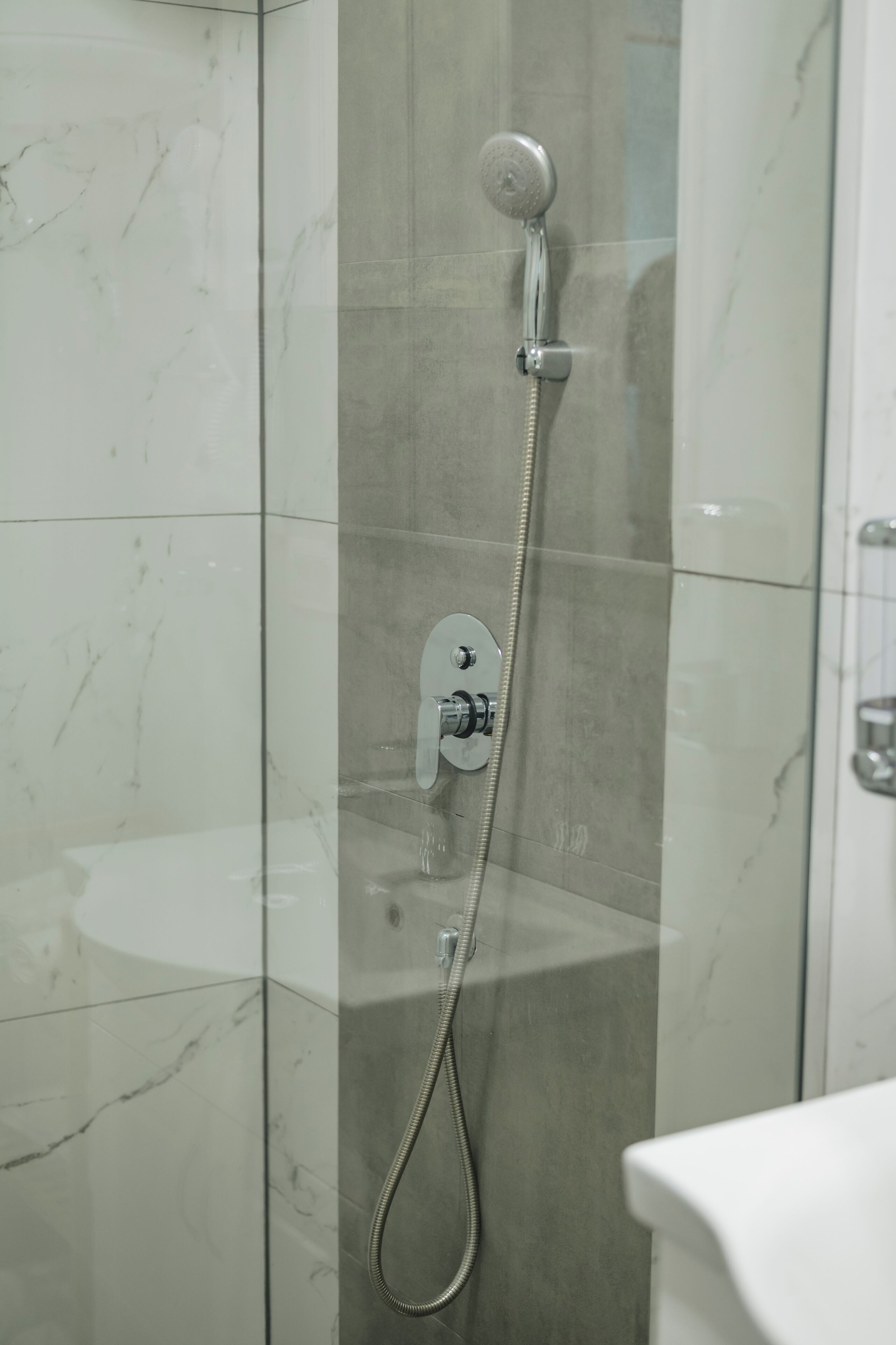 A shower with a handheld showerhead and a wall-mounted control panel.