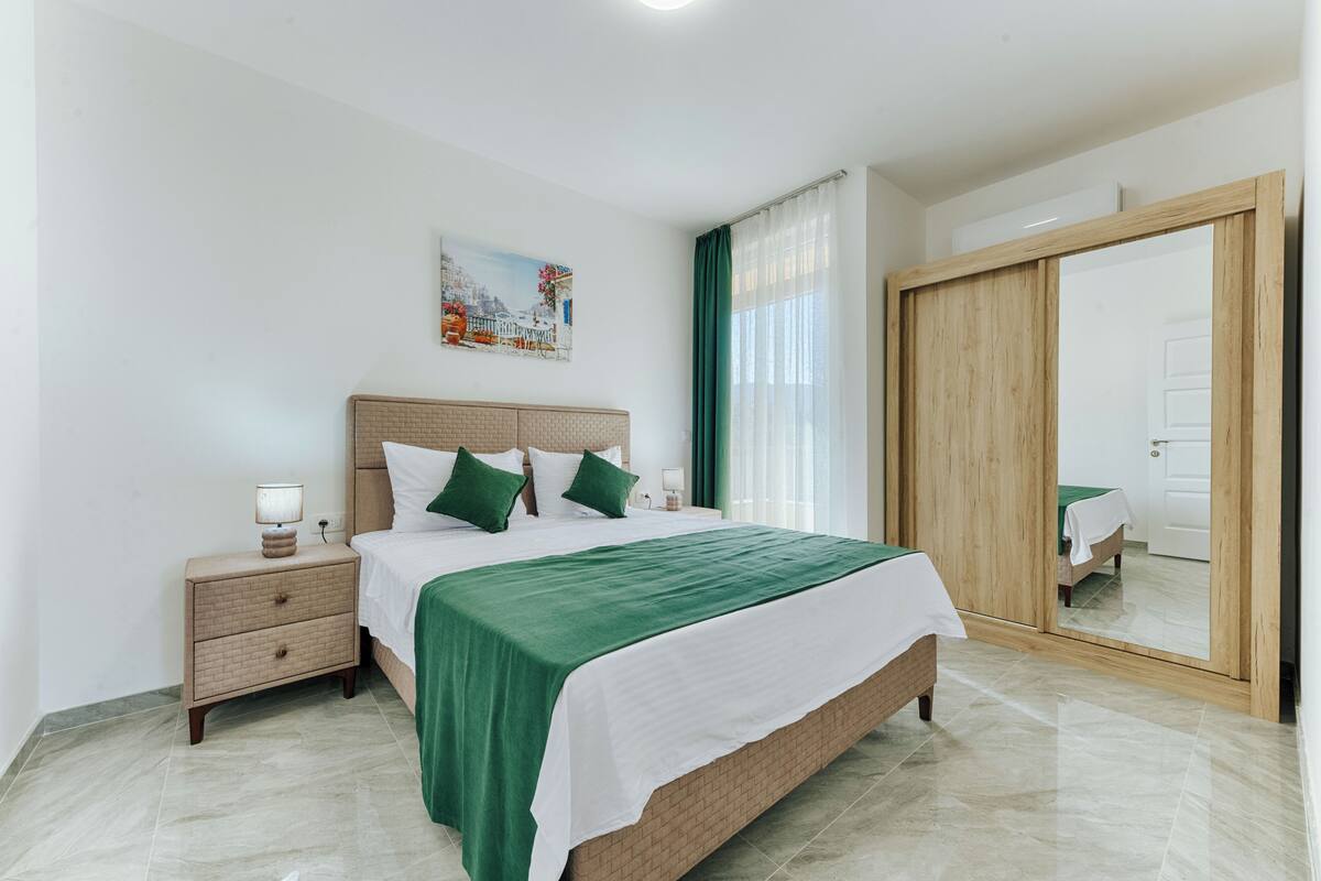 Une chambre à coucher avec un lit, une table de chevet, un miroir et un tableau accroché au mur.