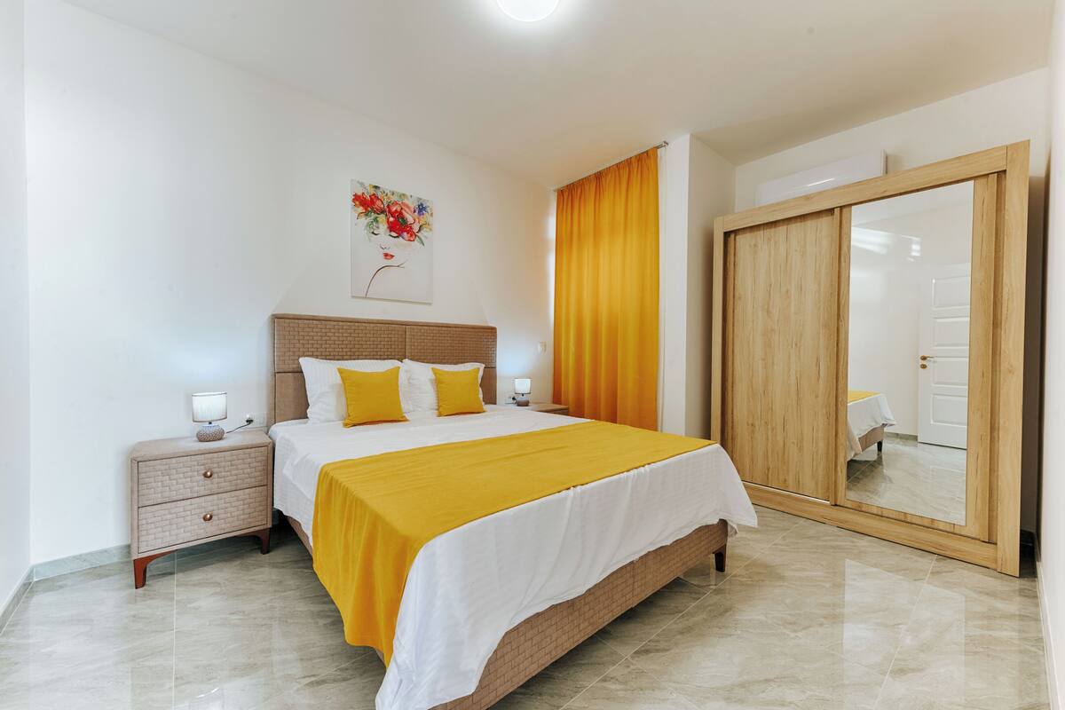 Une chambre à coucher avec un lit, des tables de chevet, un miroir et une porte.