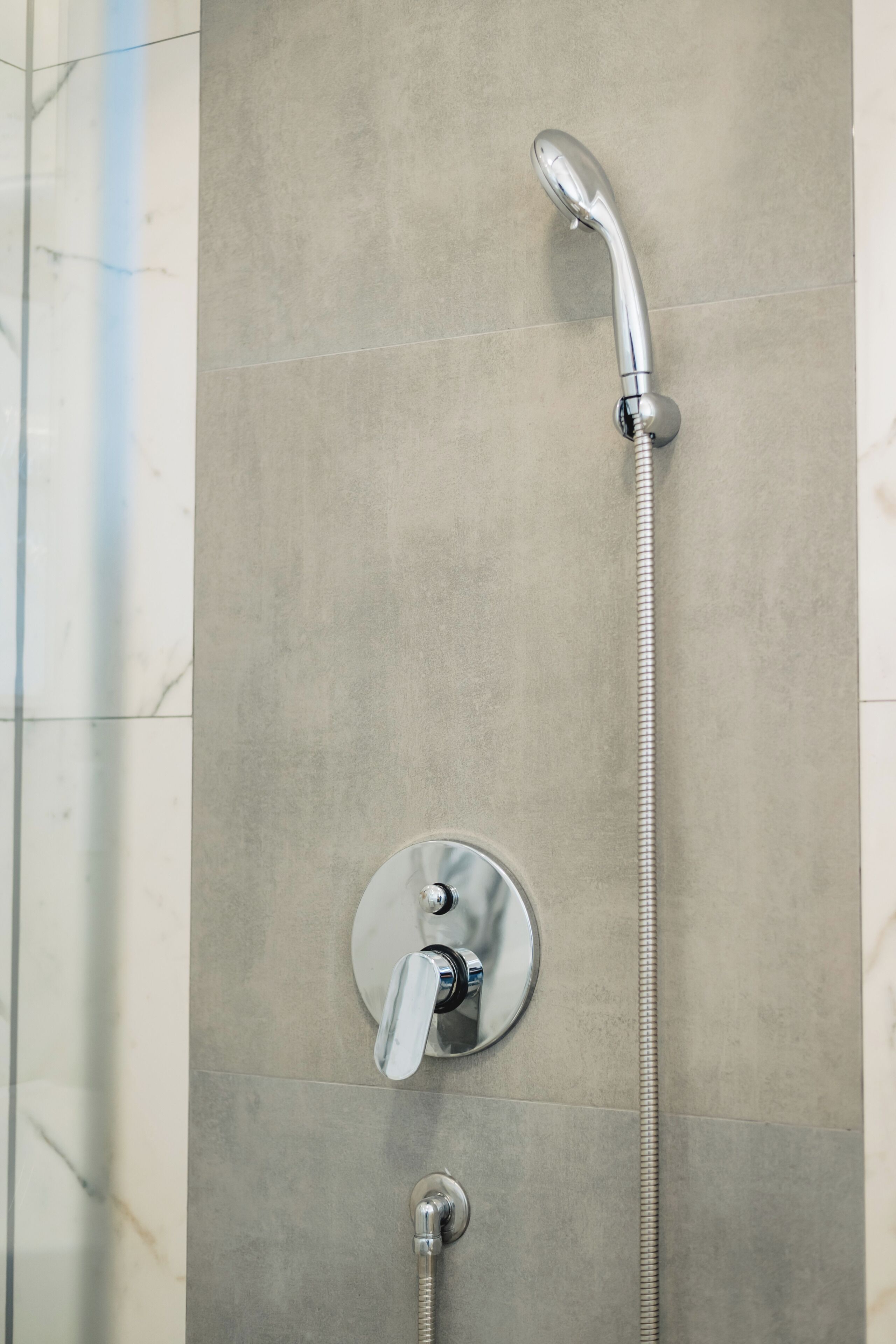 A shower with a handheld showerhead and a fixed wall-mounted faucet.