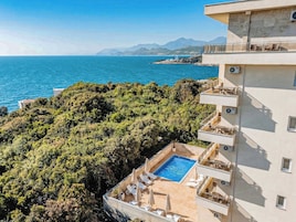 Um edifício alto com piscina no terraço, área de estar externa e vista para o mar e montanhas.