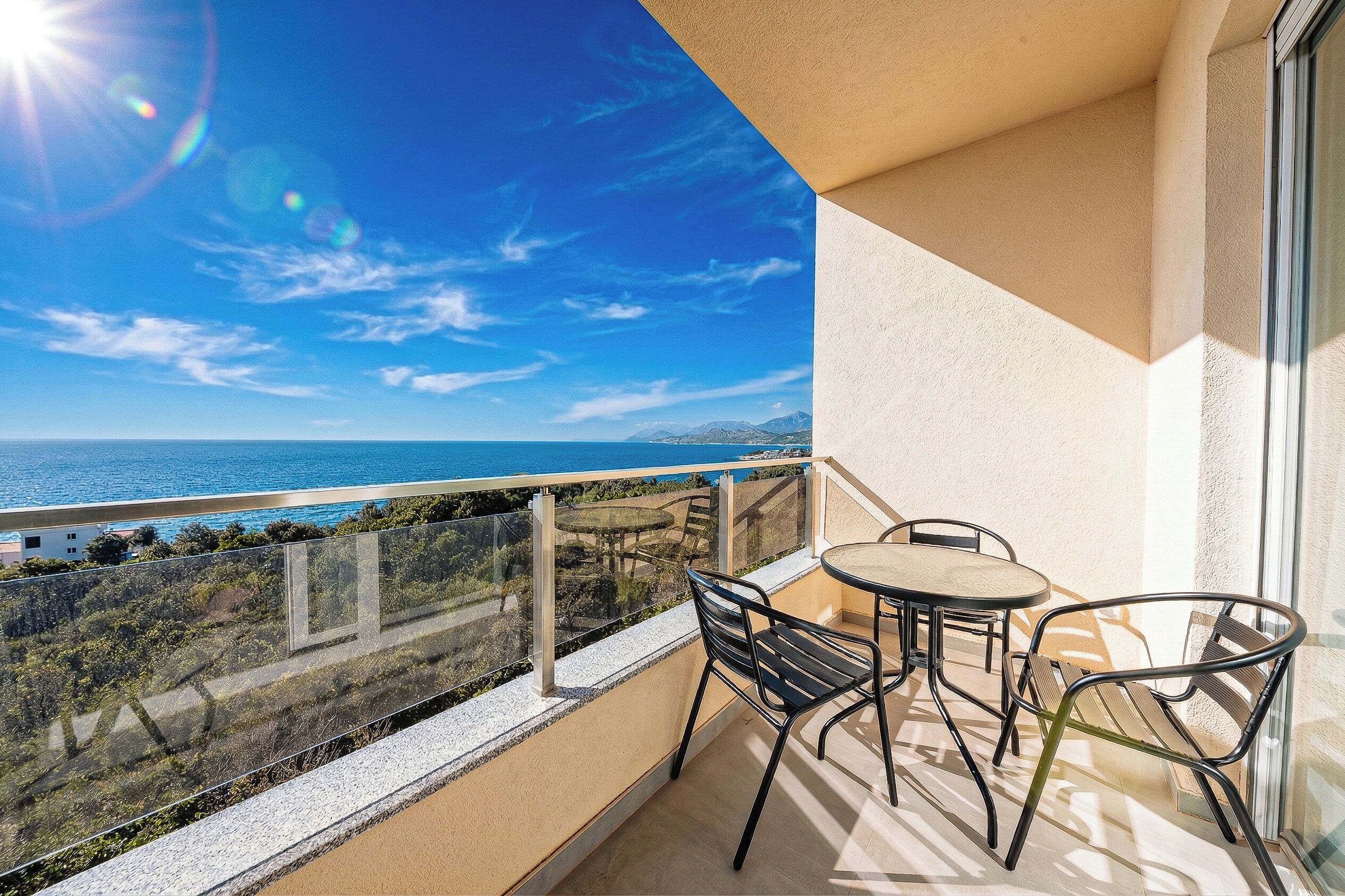 A balcony with a table and chairs, overlooking a coastal view.