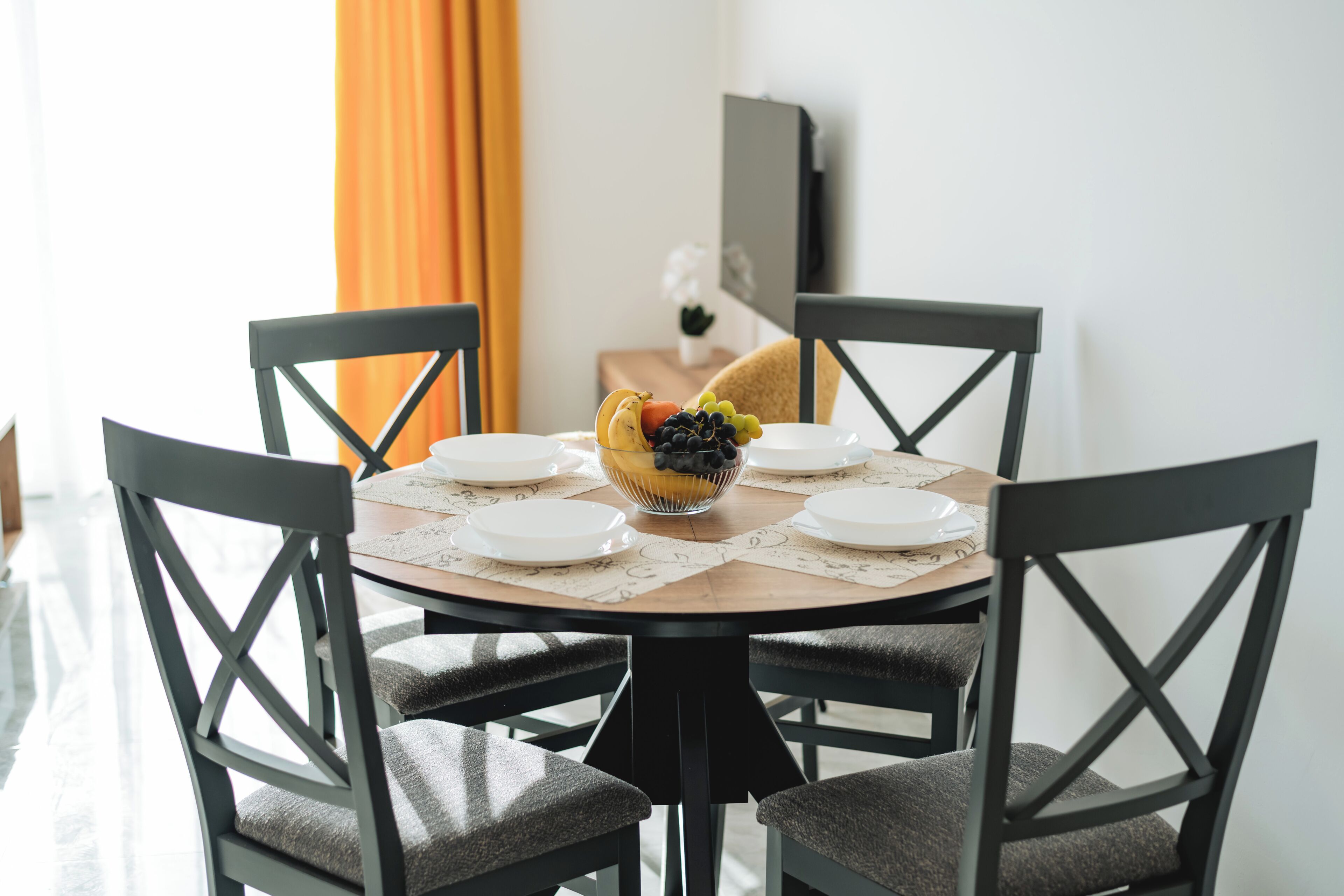 A dining table with four chairs, a bowl of fruit, and plates.