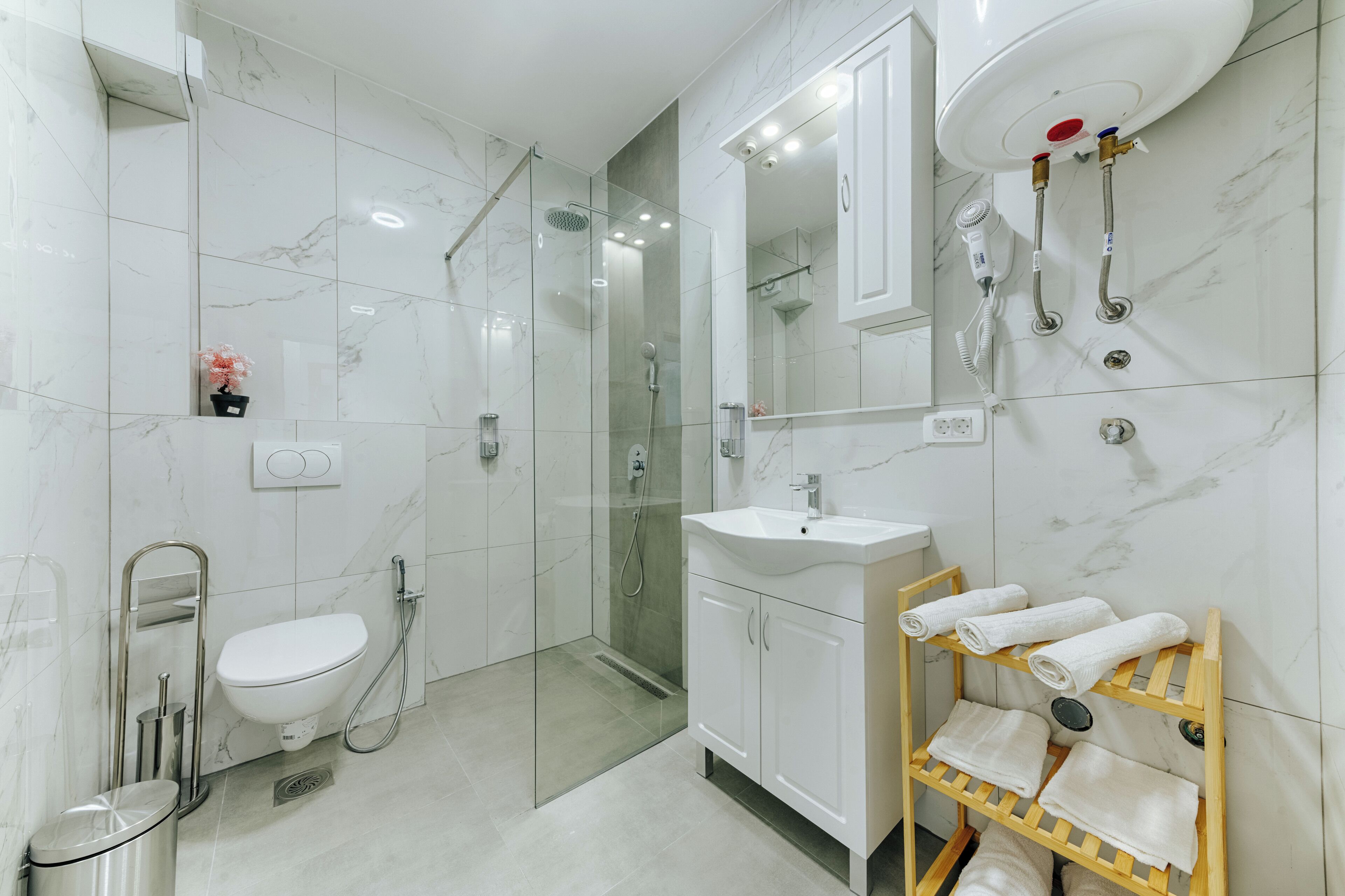 Un baño moderno con ducha envuelta en vidrio, un lavamanos blanco y un perchero de madera.