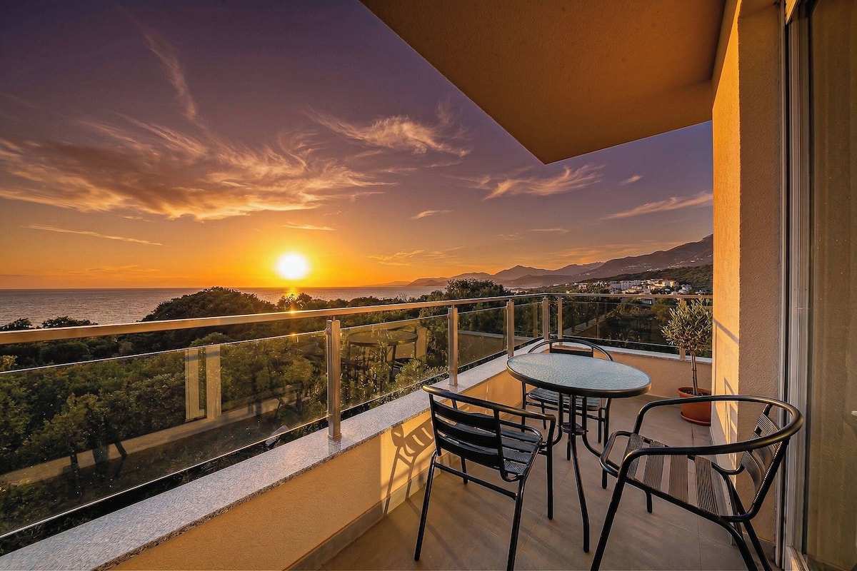 Un balcon avec une table et des chaises, offrant une vue panoramique sur le coucher du soleil et la mer.