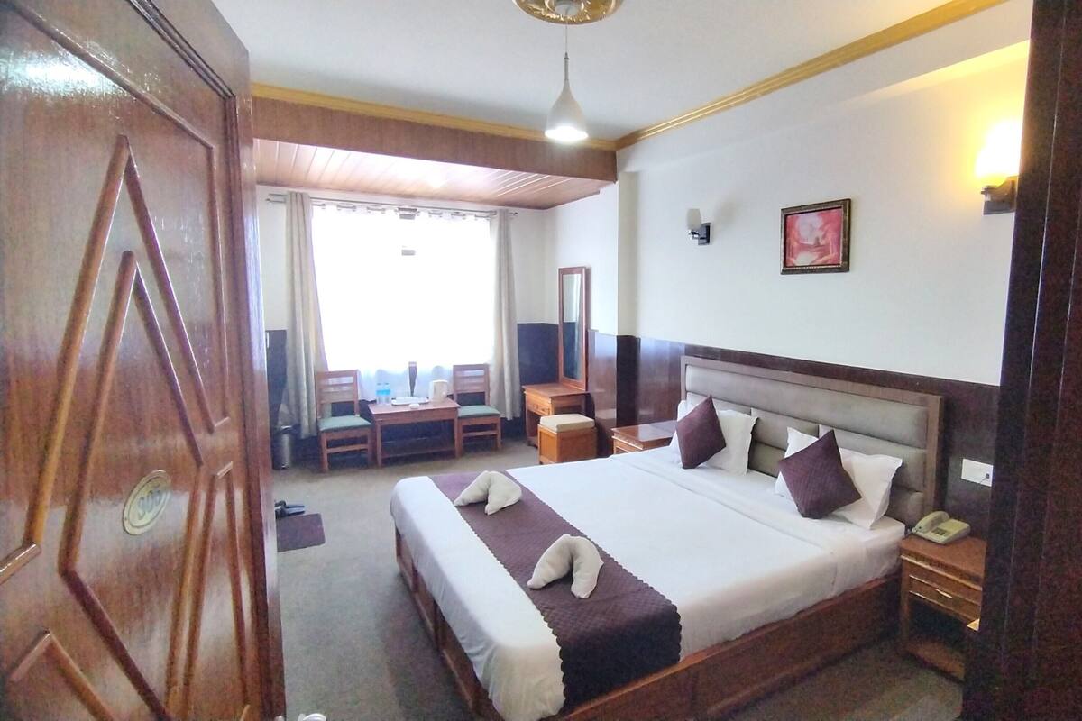 A hotel room with a large bed, bedside tables, a desk with chairs, a mirror, and a window.