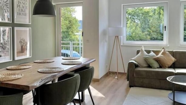 En moderne stue med et træspisebord, grønne stole, en grå sofa og en gulvlampe.