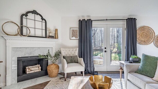 Un salon avec une cheminée, un fauteuil blanc, un canapé et une vue à travers une porte vitrée.