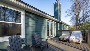 Une terrasse avec des fauteuils Adirondack, un espace salon extérieur couvert et une maison dotée d’une cheminée.