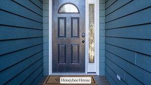 Une porte en bois sombre, dotée d’un panneau de verre, et un paillasson sur lequel on peut lire « Maison des abeilles » devant l’entrée.