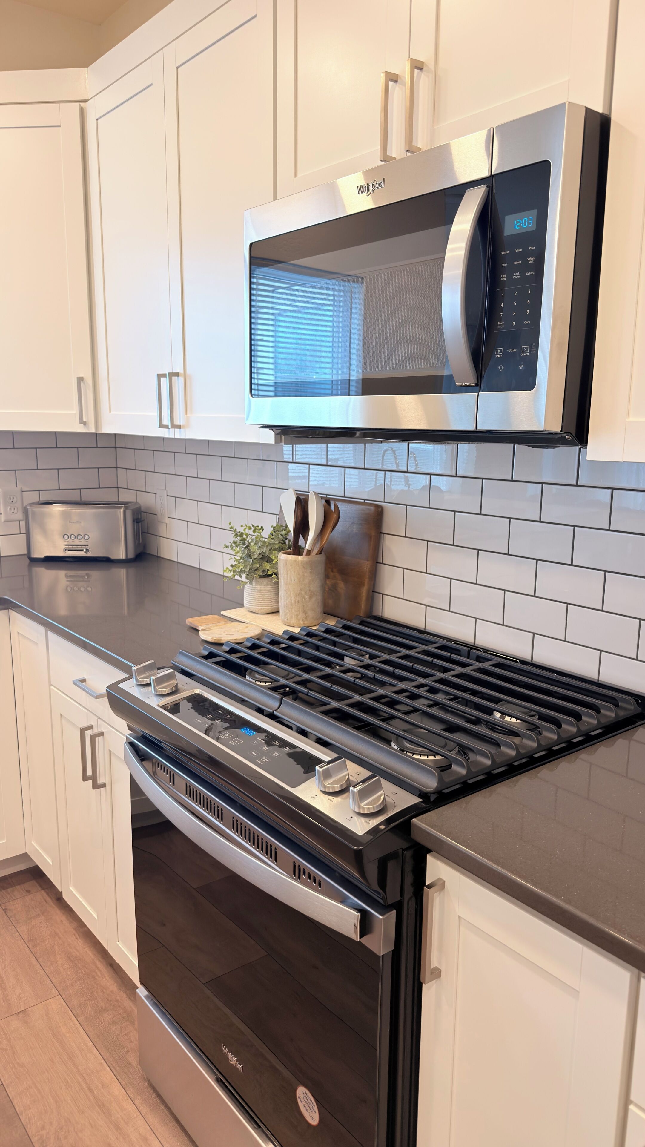 A kitchen with white cabinets, a stainless steel microwave, a toaster, and a stove.