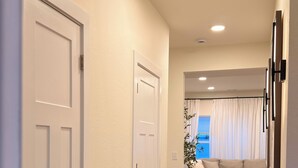 Un pasillo con piso de madera, puertas blancas, un tapete estampado y una sala de estar con sofá y cortinas.