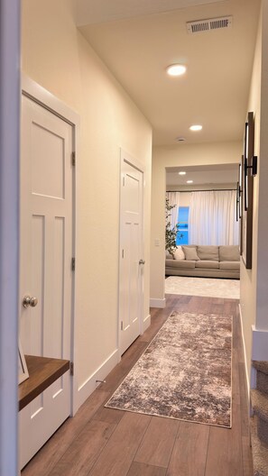 A hallway with a wooden floor, white doors, a patterned rug, and a living area with a sofa and curtains.