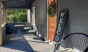 Eine Holzterrasse mit Tisch und Stühlen, einem 'WELCOME' Schild und einer Tür mit einem Kranz.