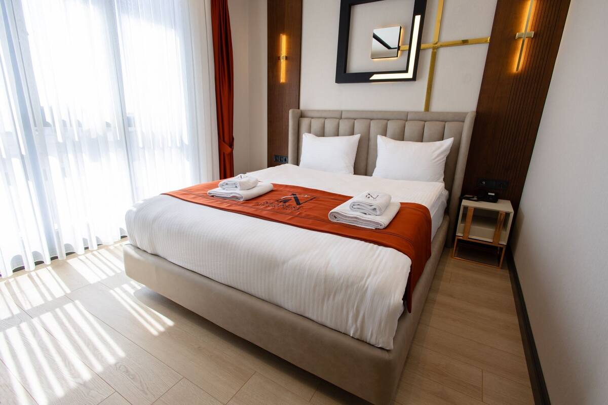 A hotel room with a large bed, a bedside table, a nightstand, and a mirror on the wall.