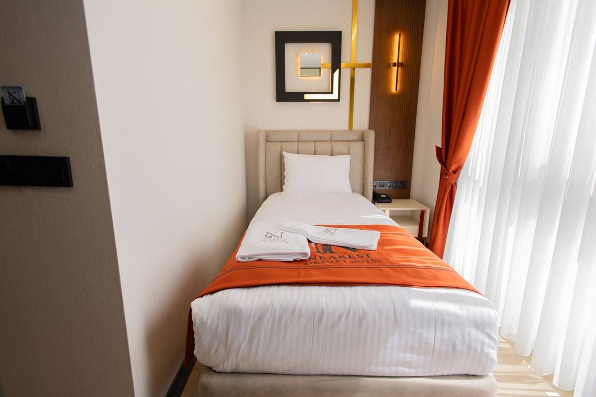A hotel room with a bed, a nightstand, a wall-mounted light, and a window with curtains.