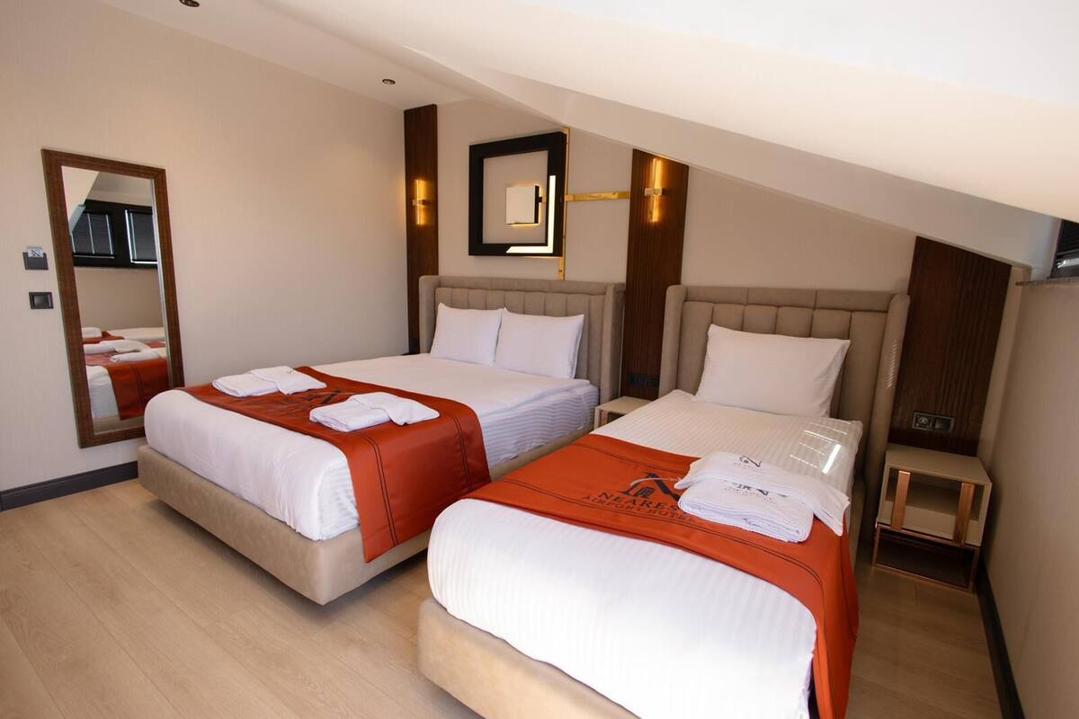 A hotel room with two beds, a mirror, a small table, and a nightstand.