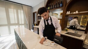 Een barista maakt koffie achter een marmeren toonbank in een goed verlichte ruimte met een groot raam en uitzicht op de stad.