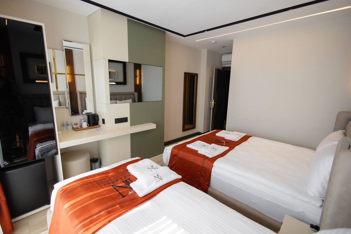 A hotel room with two beds, a desk, a mirror, and a small kitchenette.
