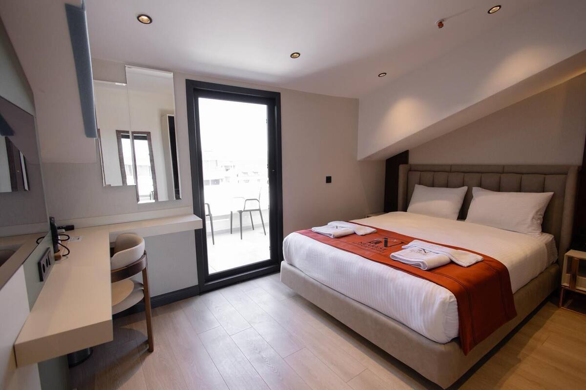 A modern hotel room with a bed, a desk, a chair, a large window, and a sliding door.