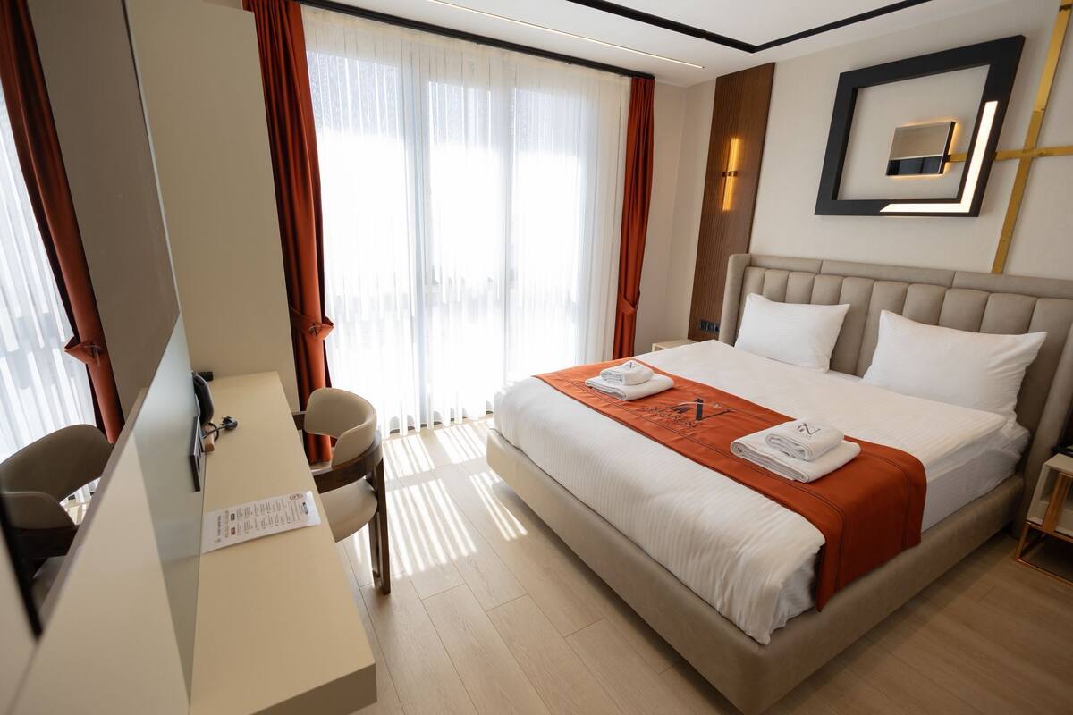 A hotel room with a bed, a desk, a chair, and a large window with curtains.