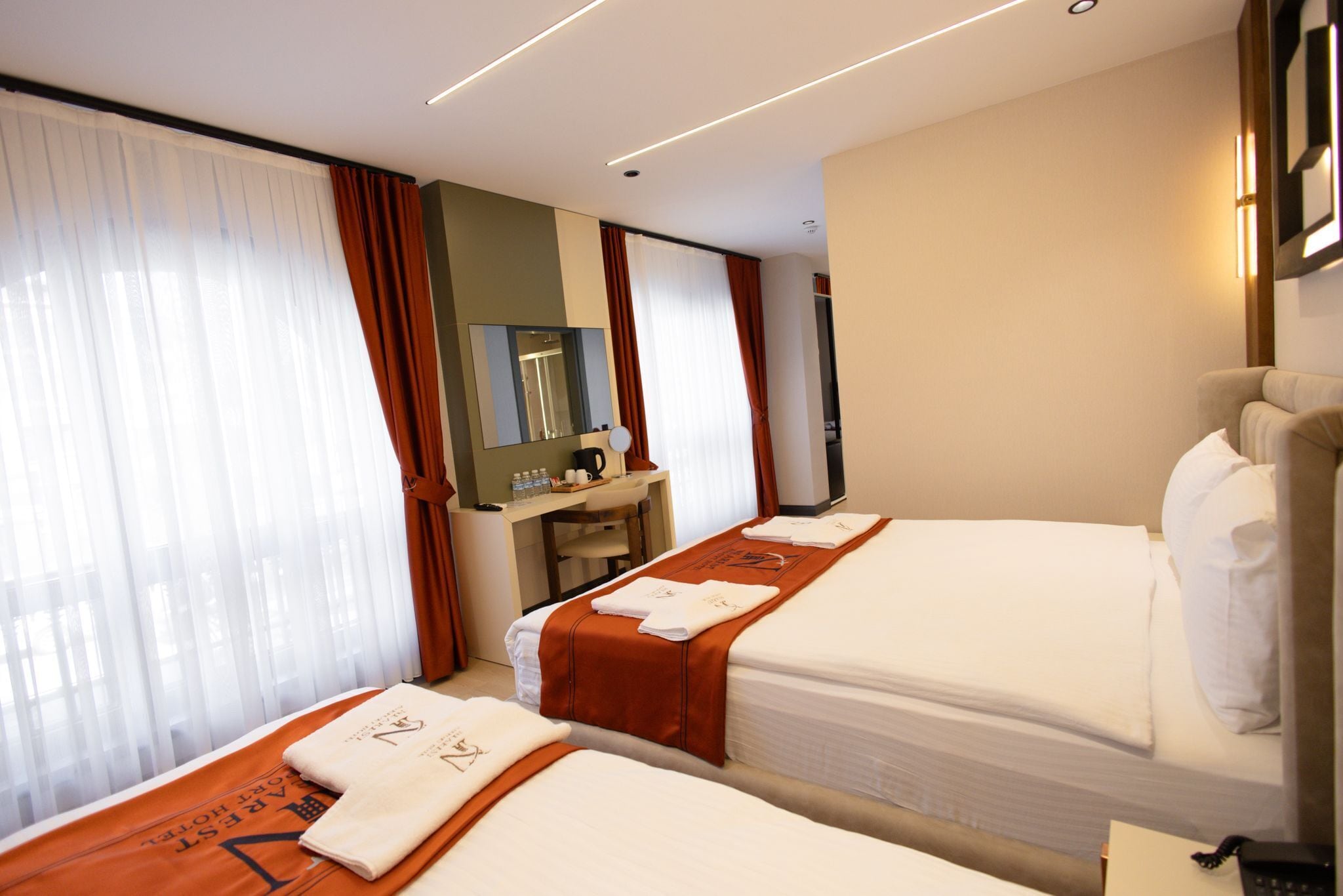 A hotel room with two beds, a desk, a mirror, and a television.