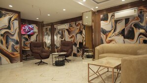 A modern living room with a marble floor, two brown armchairs, a beige sofa, a glass coffee table, and a TV mounted on the wall. - Vardaan Residency Hotel (Gorakhpur)