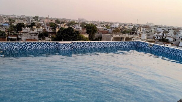 A swimming pool with a tiled edge, surrounded by a cityscape. - Vardaan Residency Hotel (Gorakhpur)