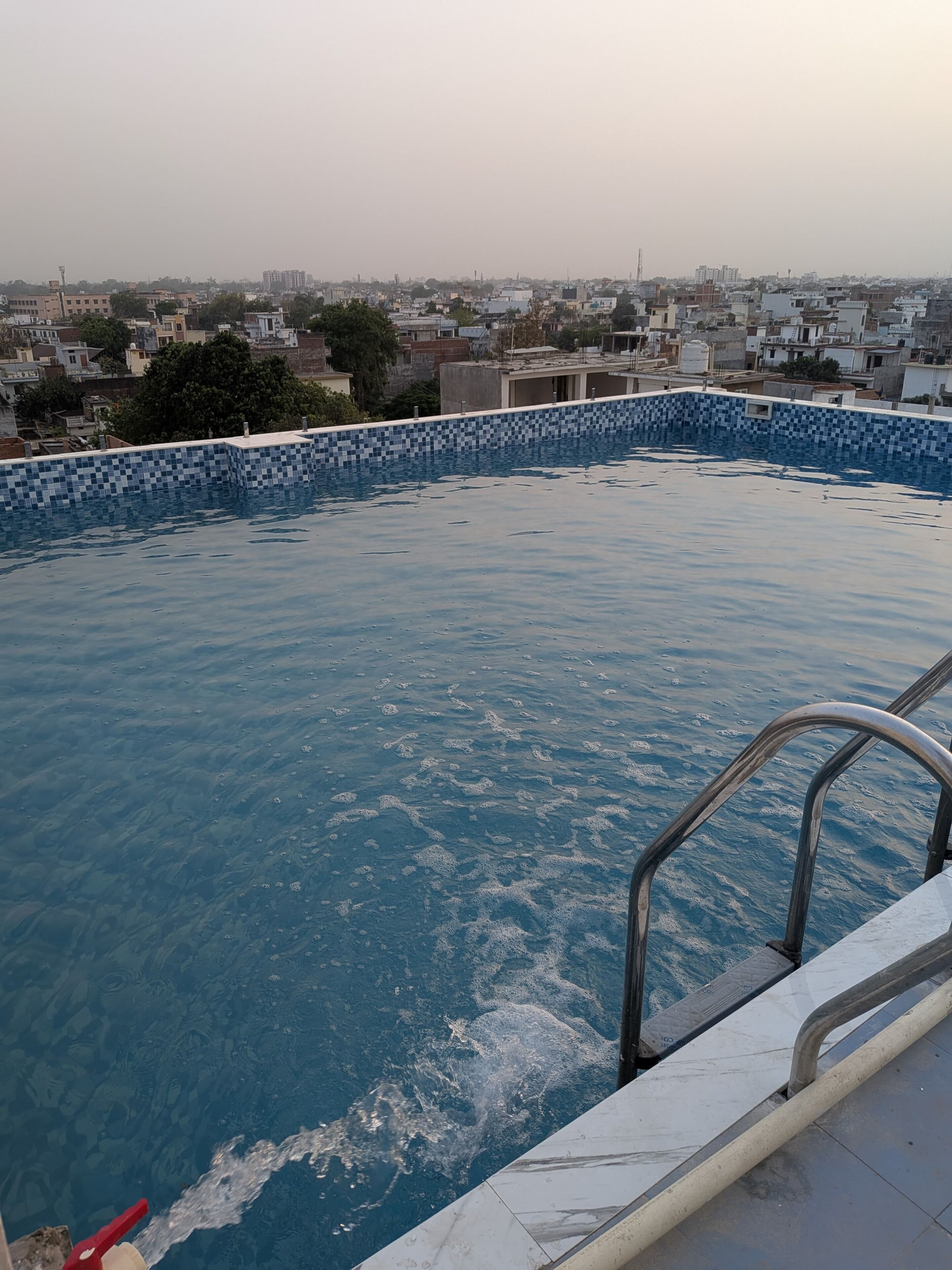 A rooftop swimming pool with a tiled edge, surrounded by a cityscape.