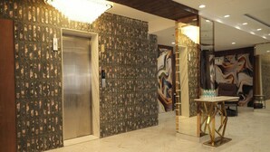 A lobby with a marble floor, an elevator, a wall with a patterned design, and a table with a modern design. - Vardaan Residency Hotel (Gorakhpur)
