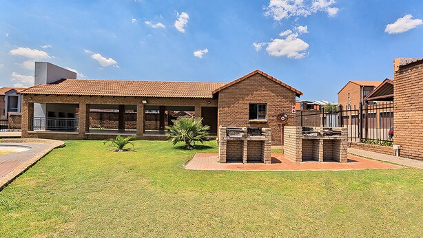 Un edificio residencial con fachada de ladrillo, un patio cubierto y una pequeña parrilla al aire libre.