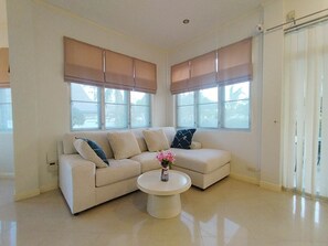 A living room with a beige sofa, a coffee table, and large windows with blinds. - Rent villa in Hua Hin (Hua Hin)
