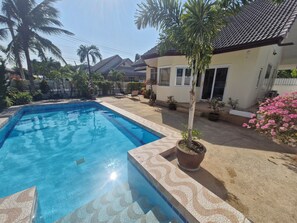 A swimming pool with tiled edges, surrounded by potted plants and a house with a tiled roof. - Rent villa in Hua Hin (Hua Hin)