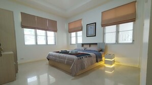 Een slaapkamer met een bed, twee nachtkastjes, een bedbankje, een ingelijst schilderij en grote ramen met zonwering.