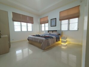A bedroom with a bed, two bedside tables, a nightstand, a framed picture, and large windows with blinds. - Rent villa in Hua Hin (Hua Hin)