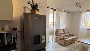 A compact living space with a modern kitchen, a leather sofa, a dining table, and a view through a window.