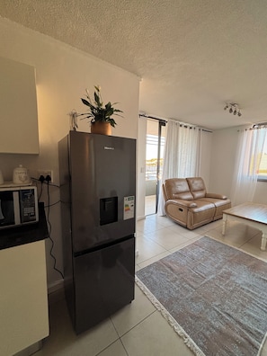 A compact living space with a modern kitchen, a leather sofa, a dining table, and a view through a window. - Cozy CBD Apartment - Windhoek (Windhoek)