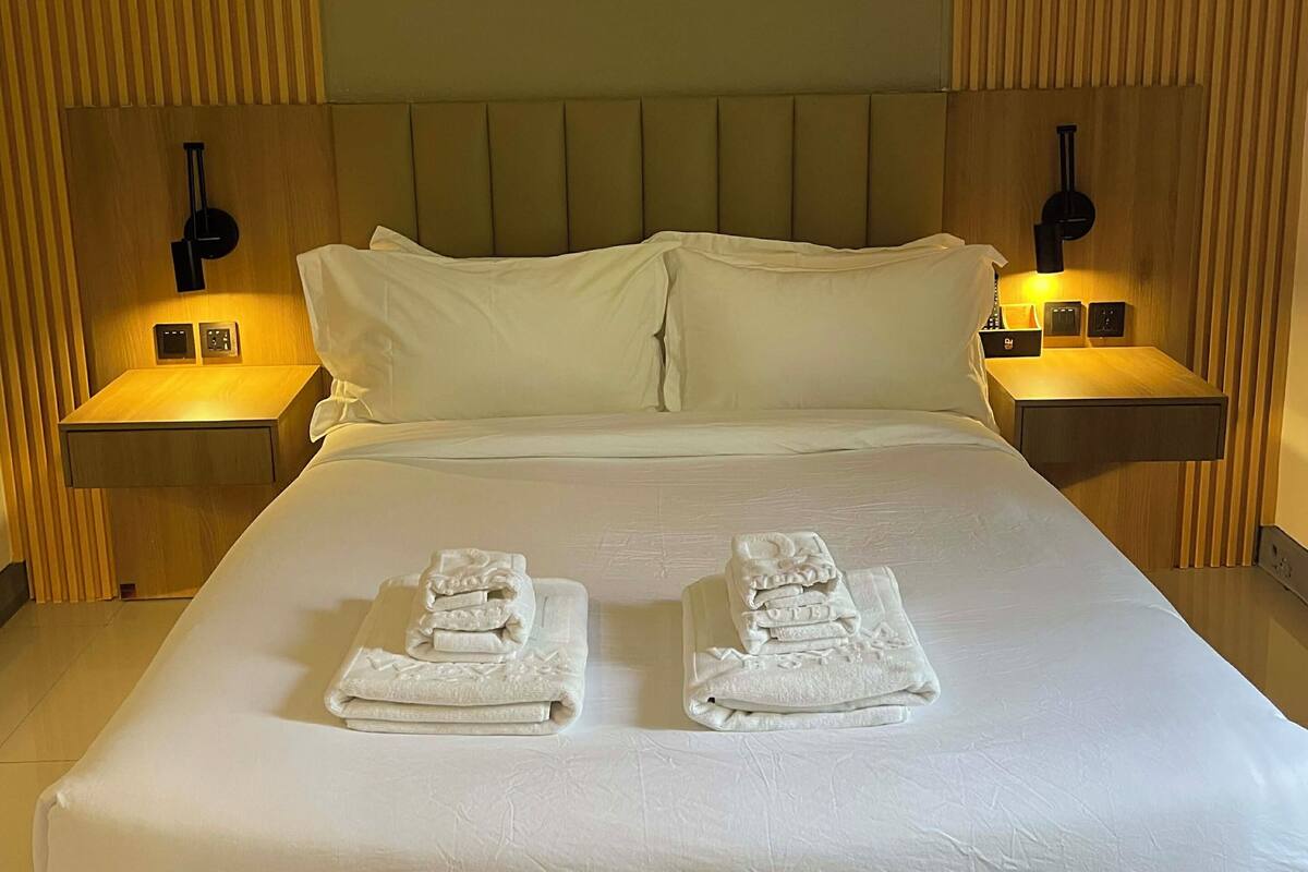 Hotellihuone, jossa on suuri sänky, kaksi yöpöytää valaisimineen ja siististi taitetut pyyhkeet sängyllä.