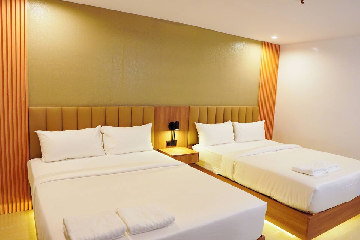 Hotellihuone, jossa on kaksi sänkyä, puinen pääty, yöpöytä lampun kanssa ja seinään kiinnitetty valaisin.
