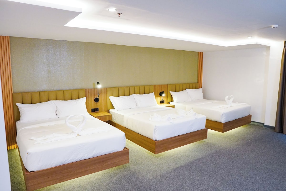 Hotellihuone, jossa on kolme sänkyä, puinen pääty ja yöpöytävalaisimet sekä neutraali v ärimaailma.