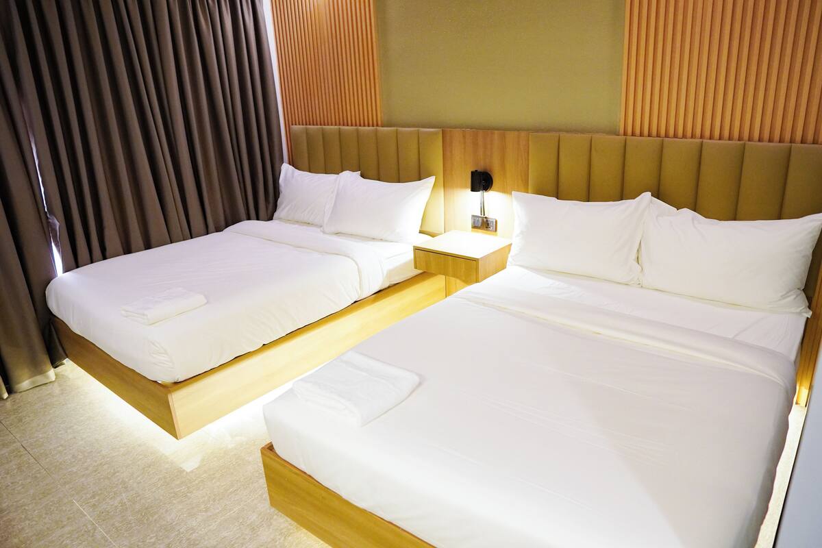 Hotellihuone, jossa on kaksi sänkyä, puinen pääty ja yöpöytä lampun kanssa sekä verho.