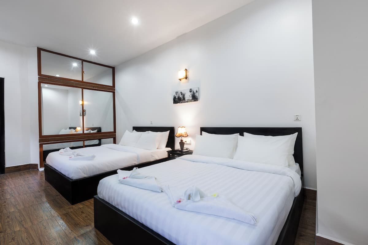 A hotel room with two beds, a large mirror, a wall-mounted picture, and a bedside table with a lamp.