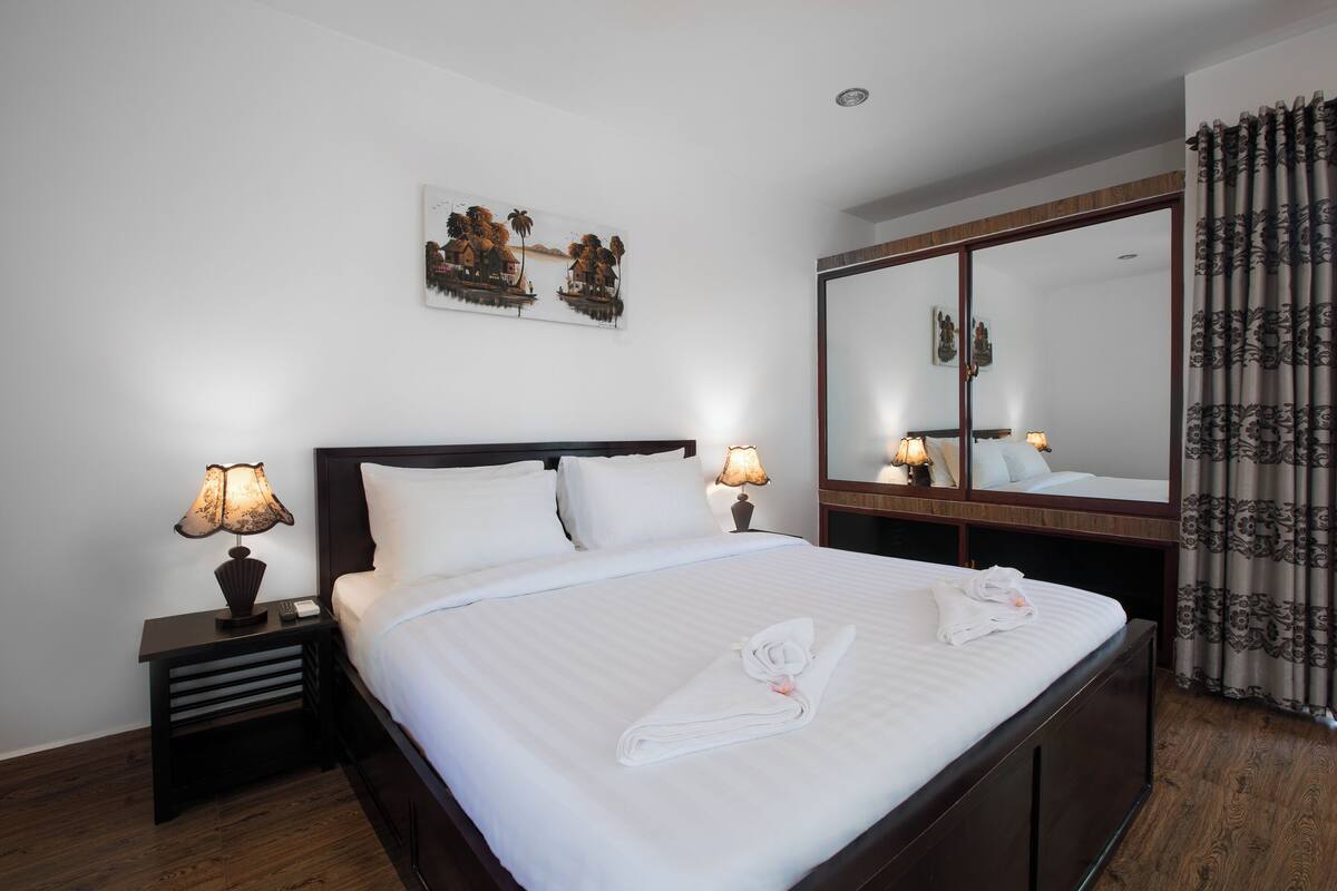 A hotel room with a large bed, two bedside tables with lamps, a mirror, and a painting on the wall.