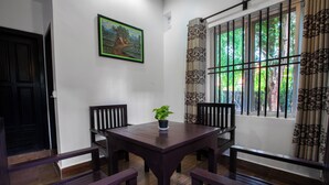Un coin repas avec une table et des chaises en bois, une plante en pot et une fenêtre avec des barreaux.
